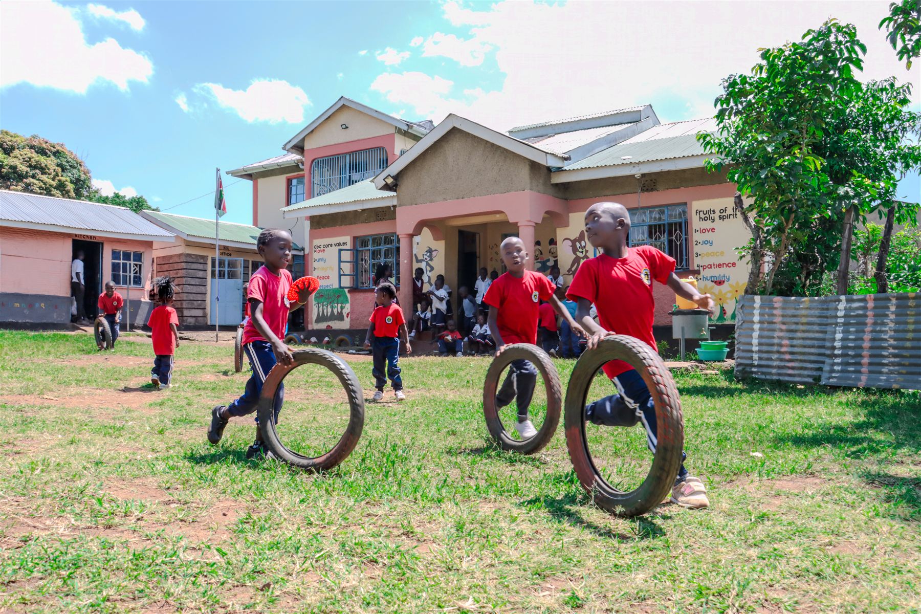 Learners in red Favoured Holman uniforms playing with tyres in front of the school building